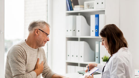 Mann fasst sich mit Schmerzen an die Brust und bespricht mit Ärztin EKG