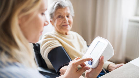 Seniorin erhält Unterstützung beim Messen des Blutdrucks