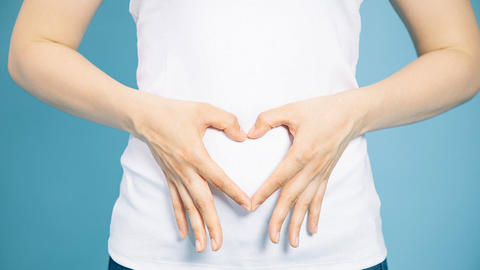 Frau formt mit Ihren Fingern ein Herz vor dem Bauch