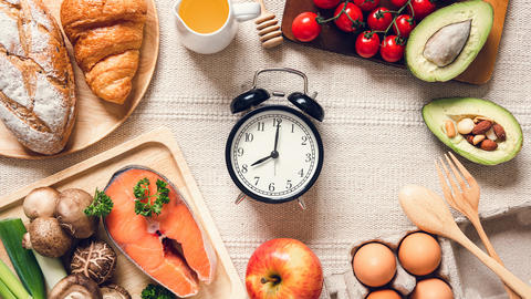 Gesunde Lebensmittel sind um einen Wecker herum arrangiert.