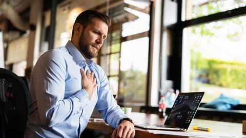 Mann fast sich am Schreibtisch an die Brust