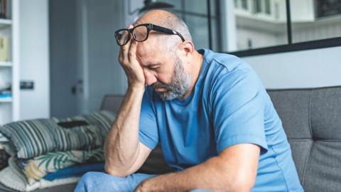 Mensch sitzt traurig im Wohnzimmer auf dem Sofa